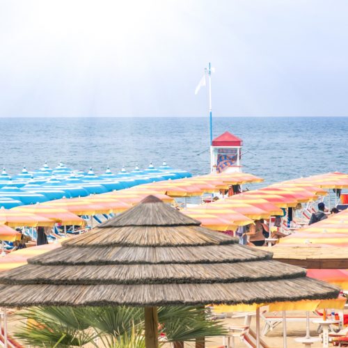 Una giornata tipo in spiaggia di Rimini in estate con file di ombrelloni colorati, lettini e il mare sullo sfondo
